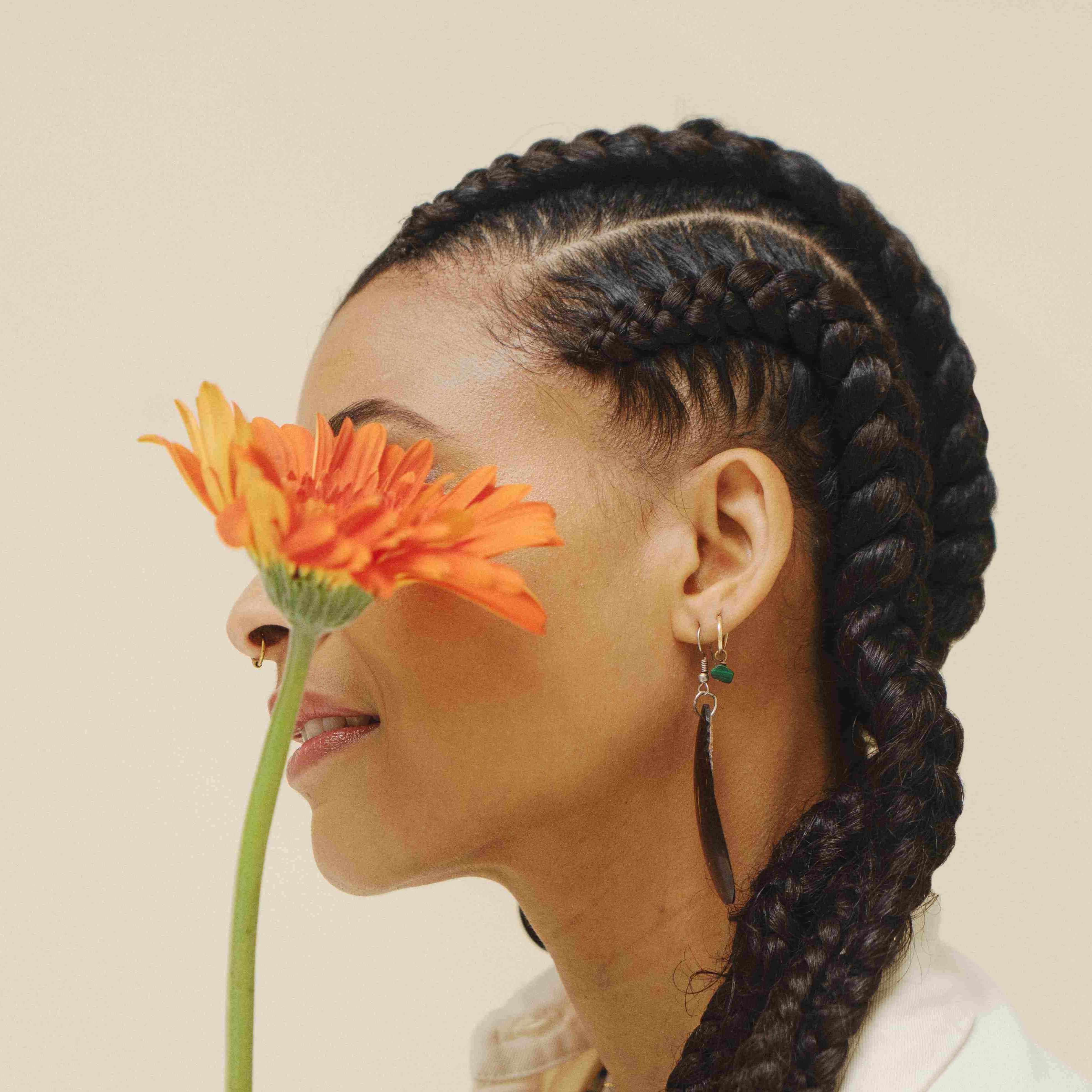 Une femme de profil a des tresses faites à partir de mèche végétales et elle tient une fleur devant son visage