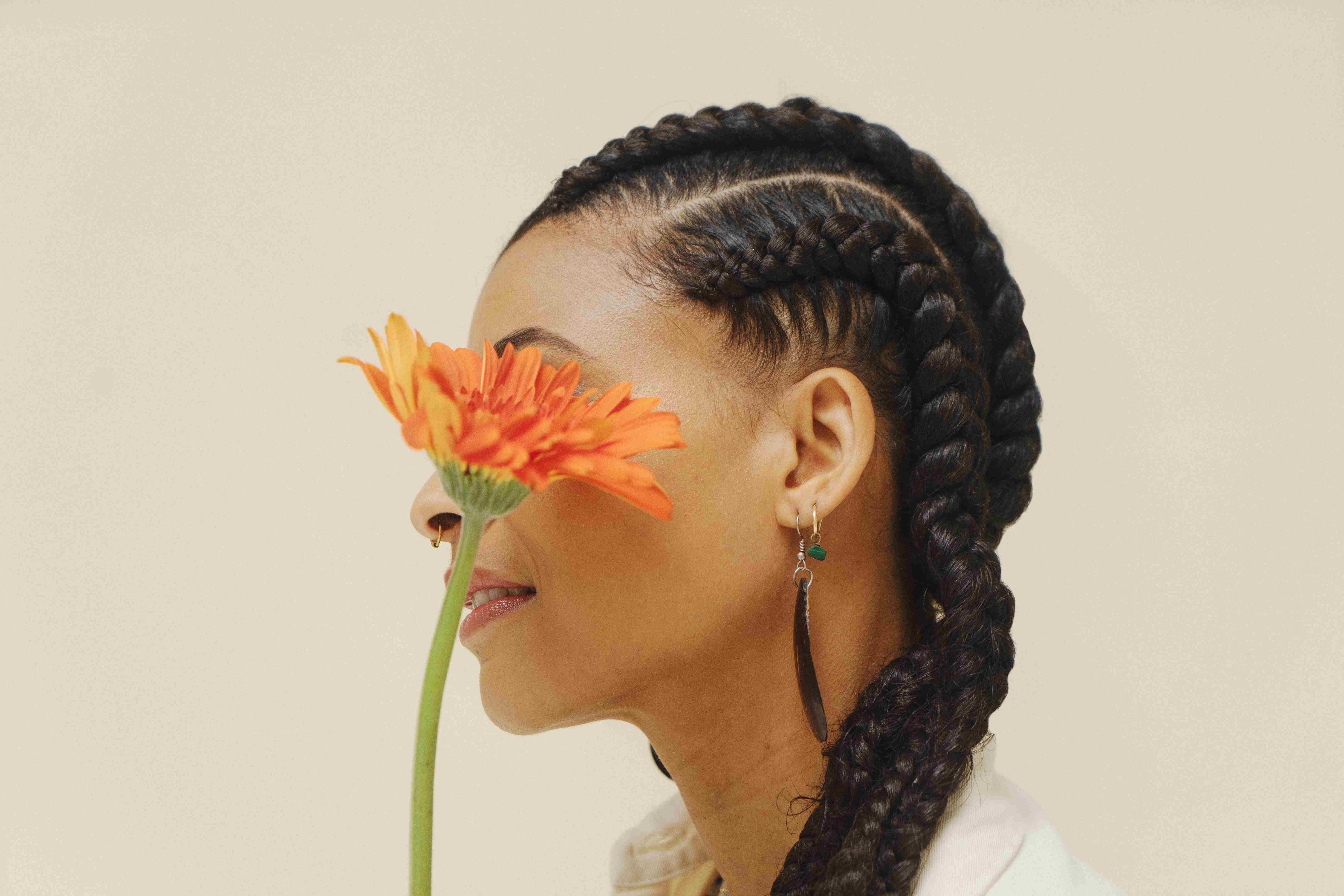 Une femme de profil a des tresses faites à partir de mèche végétales et elle tient une fleur devant son visage